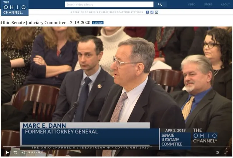 Attorney General Marc E. Dann speaking before a committee in a suit and tie.