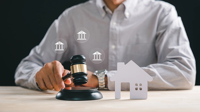 A person's hand holding gavel on block, small home model, real estate auction sale, mortgage debt, legal court proceedings, bankruptcy division.