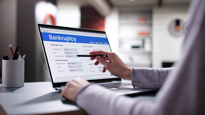Bankruptcy lawyer filling form on laptop: financial insolvency paperwork filed.