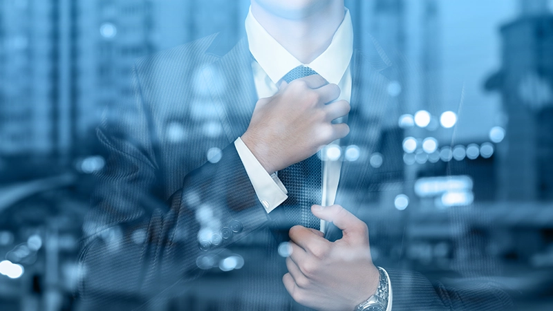 Man in a suit adjusting his tie over a blurred city skyline at night.
