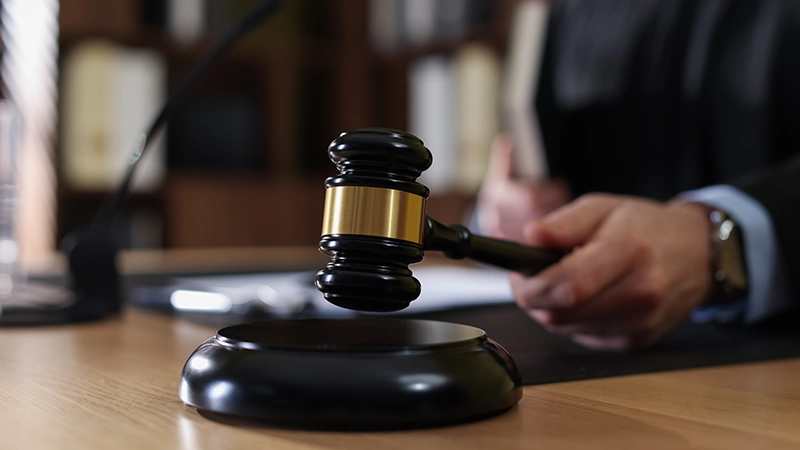 Judge striking gavel at wooden table indoors, selective focus.
