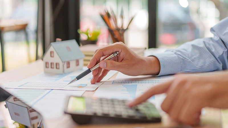 Asian male professional uses a pen and calculator to analyze property market charts.