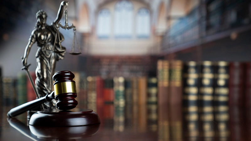 Wooden judge's gavel and Lady Justice statue on a polished table in a law library.