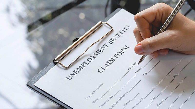 A person's hand filing written unemployment benefits application form.