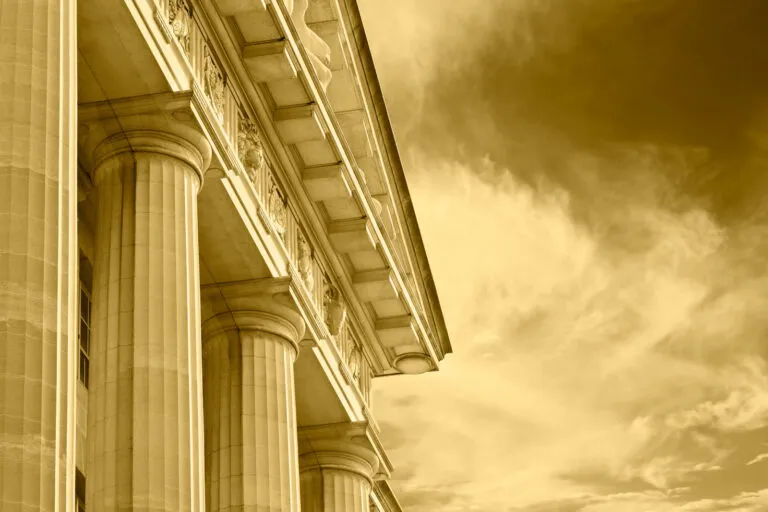 A classical stone columns on a courthouse building against a sepia-toned cloudy sky.