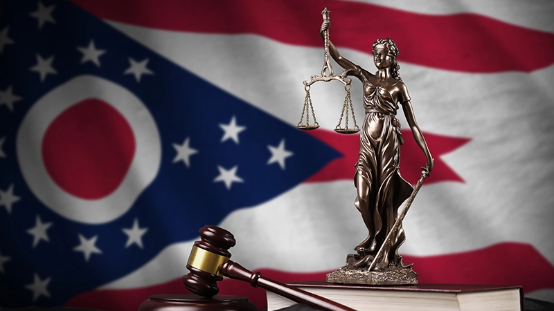 Ohio US state flag with statue of lady justice, constitution and judge hammer on black drapery.