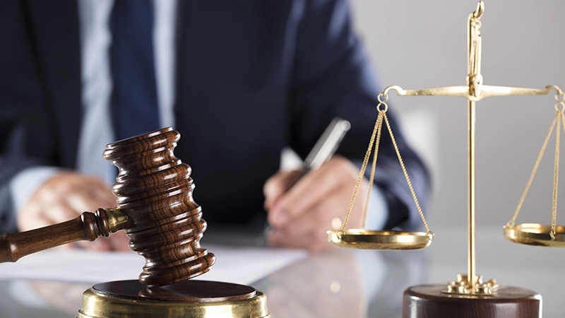 Wooden gavel and scales of justice with a blurred attorney in the background.