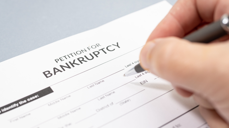 Human hand with pen filling a bankruptcy form on table.